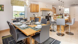 A modern kitchen with wooden cabinets, a dining area with a glass table, and a view of the outdoors. - 3 bedroom accommodation in Dunbeath, near Wick (Dunbeath, near Wick)
