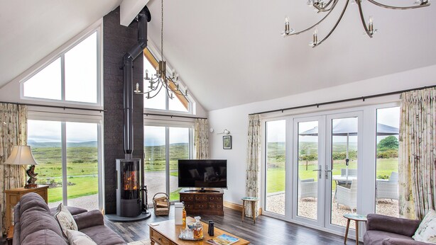 A spacious living room with a fireplace, a television, and a large window overlooking a scenic landscape. - 3 bedroom accommodation in Dunbeath, near Wick (Dunbeath, near Wick)