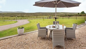 A round table with wicker chairs and a large umbrella, set on a gravel patio with a view of rolling hills. - 3 bedroom accommodation in Dunbeath, near Wick (Dunbeath, near Wick)