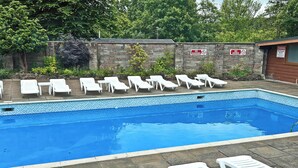 A swimming pool with white lounge chairs and a stone wall with warning signs. - Twit Too Woo - UK6760 (Cenarth, near Newcastle Emlyn)