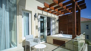 Un balcone moderno con ringhiera in vetro, una sedia bianca, un tavolino rotondo e una vasca da bagno ampia.