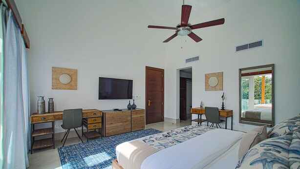 A bedroom with a bed, desk, chair, television, and a ceiling fan. - Owner-Rented Contemporary All-Inclusive Tropical Villa (Puerto Plata)