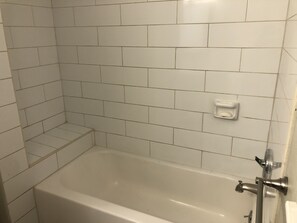Une salle de bain aux murs recouverts de carreaux blancs, avec une baignoire, un porte-savon et un robinet de douche.
