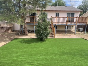 Un jardin avec une terrasse en bois, un petit arbre et une pelouse bien entretenue.
