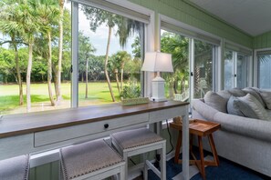 Une chambre avec vue sur un terrain de golf, un bureau avec une lampe, un canapé et un petit tabouret en bois.