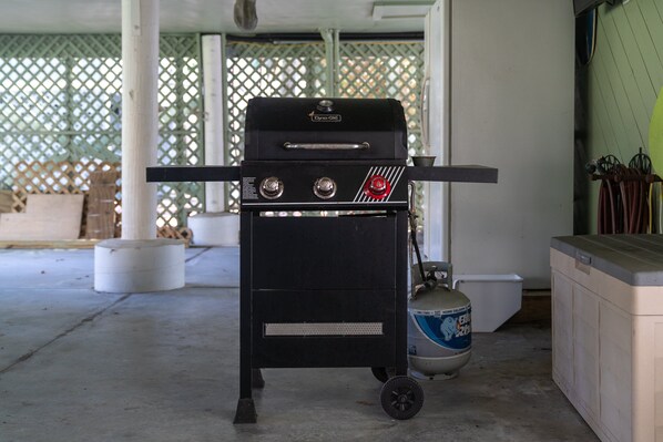 Un barbecue portatif doté de deux brûleurs et d’un bouton de réglage, placé sur un sol en béton, avec une bouteille de gaz à proximité.