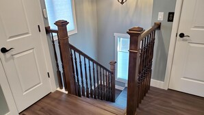 Un escalier en bois, doté d’une rampe, mène à un palier où se trouvent une fenêtre et une porte.