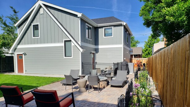 Une maison à deux étages dotée d’un patio aménagé avec du mobilier d’extérieur et une clôture en bois.
