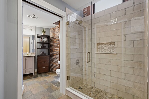 A bathroom with a glass-enclosed shower, a brick accent wall, and a vanity with a mirror.