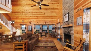 A cozy cabin interior with a fireplace, wooden floors, a leather sofa, and a dining area. - Steamy Soaks with Scenic Views, Fireside Chats, Outdoor Showers & Game Nights - Jackson's Cabin (Sevierville)