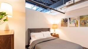A bedroom with a bed, bedside tables, a lamp, and artwork on the wall. - Fresh, Sleek, and Contemporary Executive Apartment (Rochester)
