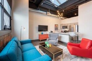 A modern living room with a blue sofa, a red chair, and a coffee table. There is a kitchen area with a microwave and a refrigerator. - Fresh, Sleek, and Contemporary Executive Apartment (Rochester)