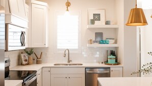 A modern kitchen with white cabinetry, a stainless steel dishwasher, and a window with blinds. - North Hampton | Pool, Hot Tub & Family-Friendly Spaces Near St. George (Washington)