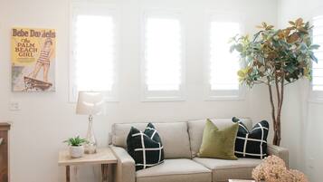 A living room with a beige sofa, a small table with a lamp, and a poster on the wall.
