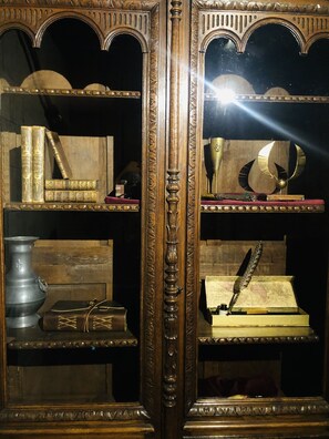 A wooden cabinet with ornate carvings and shelves holding books, a quill, and a decorative globe.