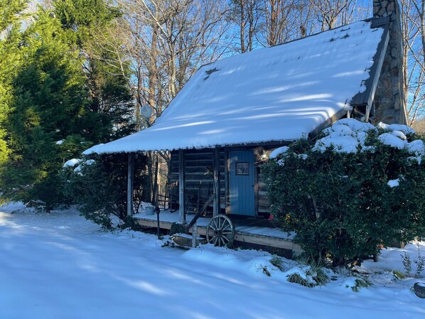 A log cabin with a snow-covered roof, a porch with a wagon wheel, and a number '321' on the door.