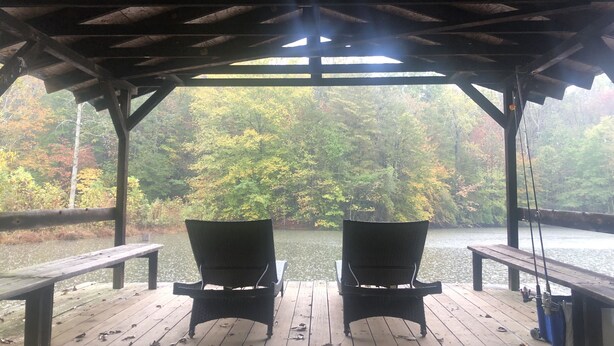 En överbyggd träveranda med två stolar som vetter mot en sjö omgiven av träd.