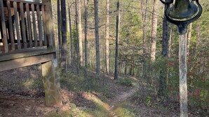 Ett trädäck med en stenmur, omgivet av en skog med en metallklocka som hänger på en stolpe.
