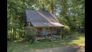 En enkel stuga med ett sluttande tak, en veranda och en liten trädgård framför huset.
