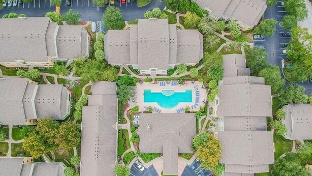 Ett flygbildsbild av ett bostadsområde med flera hus, en central pool och en rundad uppfart.