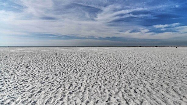 Ein weiter, sandiger Strand mit blauem Himmel.