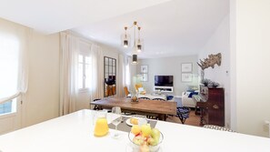 Een moderne eethoek met een houten tafel, witte stoelen en een schaal fruit.