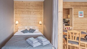 Ett rum med träpanel på väggarna, en säng, två sänglampor, en stol och ett litet pentry som syns genom en öppen dörr.