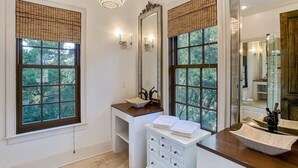 Une salle de bain avec deux fenêtres, un meuble-lavabo avec un évier, un miroir et un lustre.