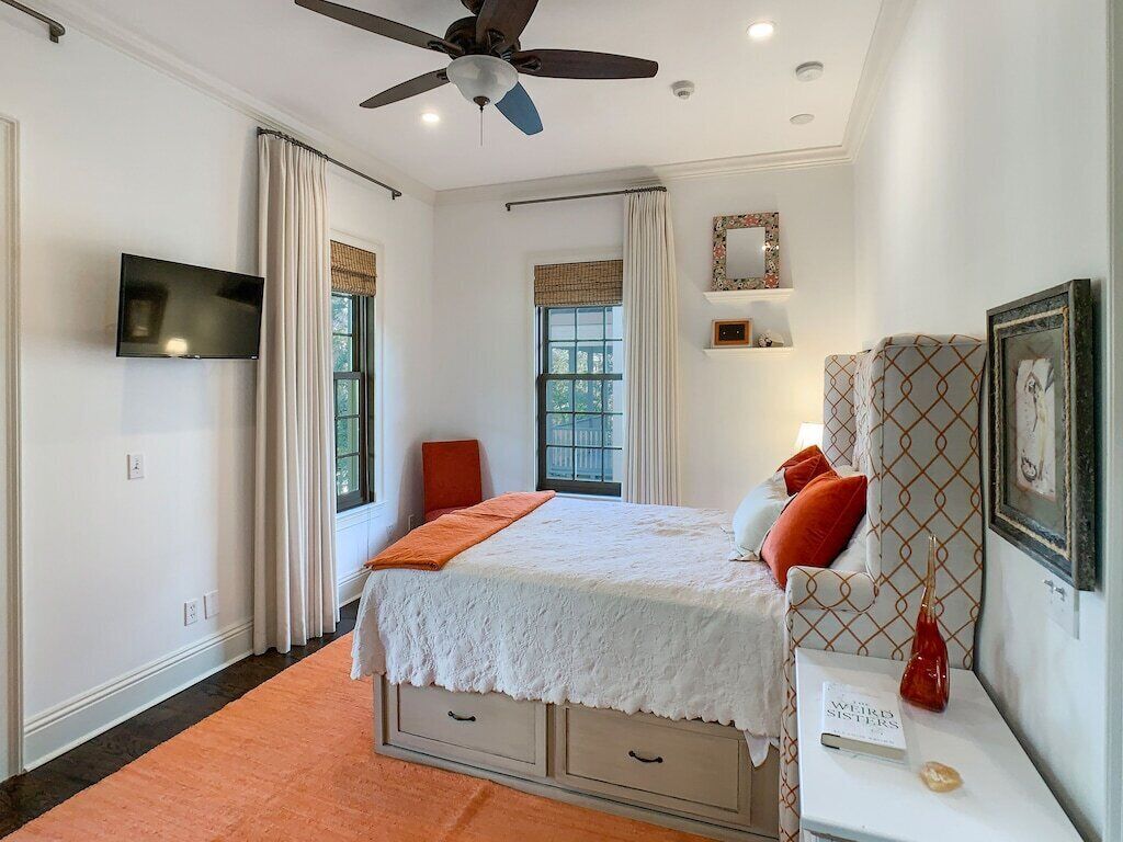 A bedroom with a bed, a TV, a ceiling fan, and a window with curtains.
