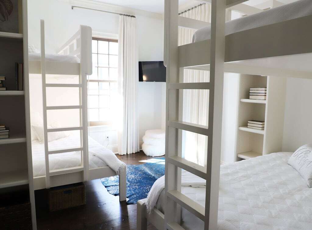 A room with bunk beds, a flat-screen TV mounted on the wall, and a window with curtains.