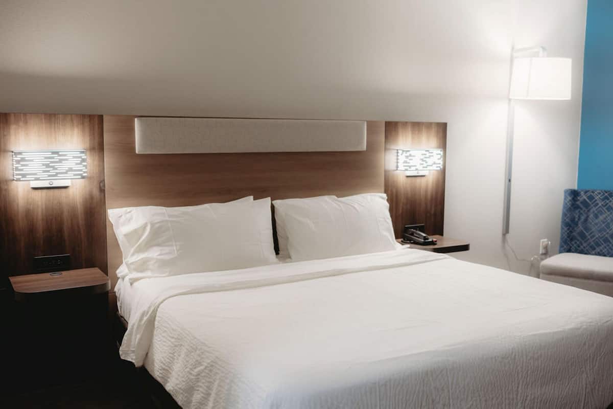 A hotel room with a large bed, bedside tables, a nightstand, a wall-mounted lamp, and a blue accent wall.