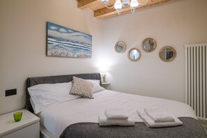 Een slaapkamer met een bed, kussens, een nachtkastje, een groen glas, een schilderij en drie ronde spiegels aan de muur.