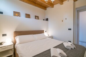 A bedroom with a bed, bedside table, lamp, and a wall-mounted shelf with decorative items.
