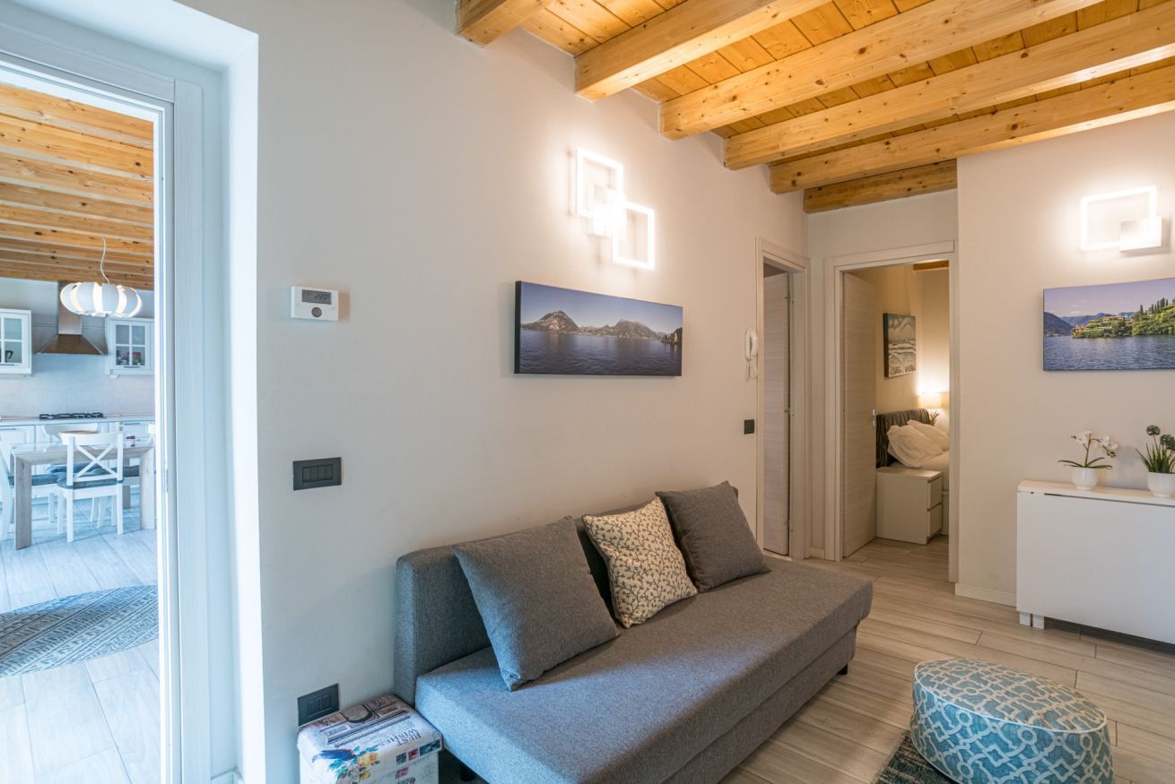 Una sala de estar moderna con un sofá gris, vigas de techo de madera y dos lámparas fijadas a la pared.