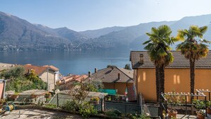 A residential area with a view of a lake and mountains, featuring houses with tiled roofs and a palm tree. - GuestHost - Apartment of about 80 sqm, perfect for 4/6 people (but it can host up to 7 people), located in a pedestrian area, on the ground floor of a renovated house overlooking Lake Como. The property is located in the historic centre of the enchanting (Carate Urio)