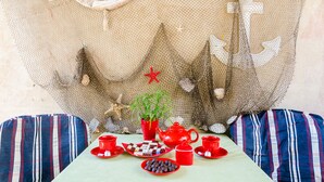 Una mesa dispuesta con tetera roja, tazas y dulces, una planta en maceta y un fondo decorativo con un barco y un ancla.