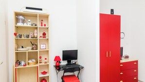 Una habitación con una estantería de madera, un armario rojo, un escritorio con una computadora y una silla roja.