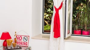 Una habitación con ventana, un cartel de 'No Fumar', una lámpara roja y una mesa de vidrio con aperitivos.