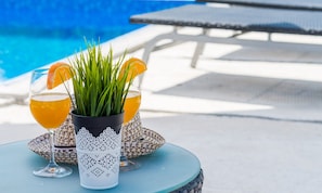 Two glasses of orange juice with a potted plant and a decorative item on a table by a pool.
