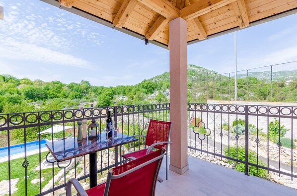 A balcony with a table and chairs, overlooking a pool and greenery.