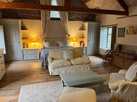 Un dormitorio acogedor con cama dosel, una zona de estar con un banco y suelo de madera.