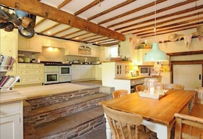 A cozy kitchen with a stone staircase, wooden beams, and a wooden dining table.