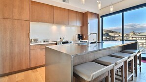 A modern kitchen with a large island, wooden cabinets, and a view of the city through large windows.