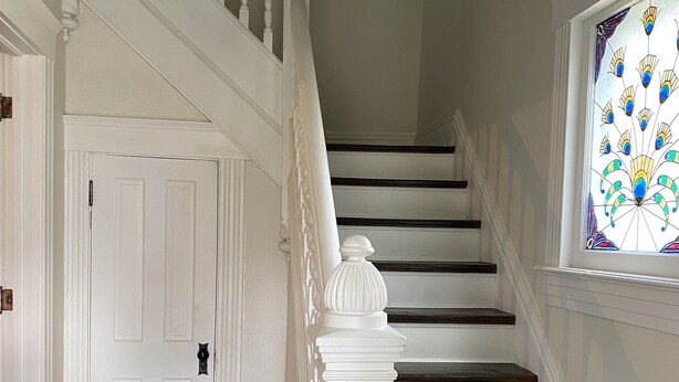 Un escalier avec des balustrades blanches et des marches sombres, menant à une porte dotée d’une poignée noire.