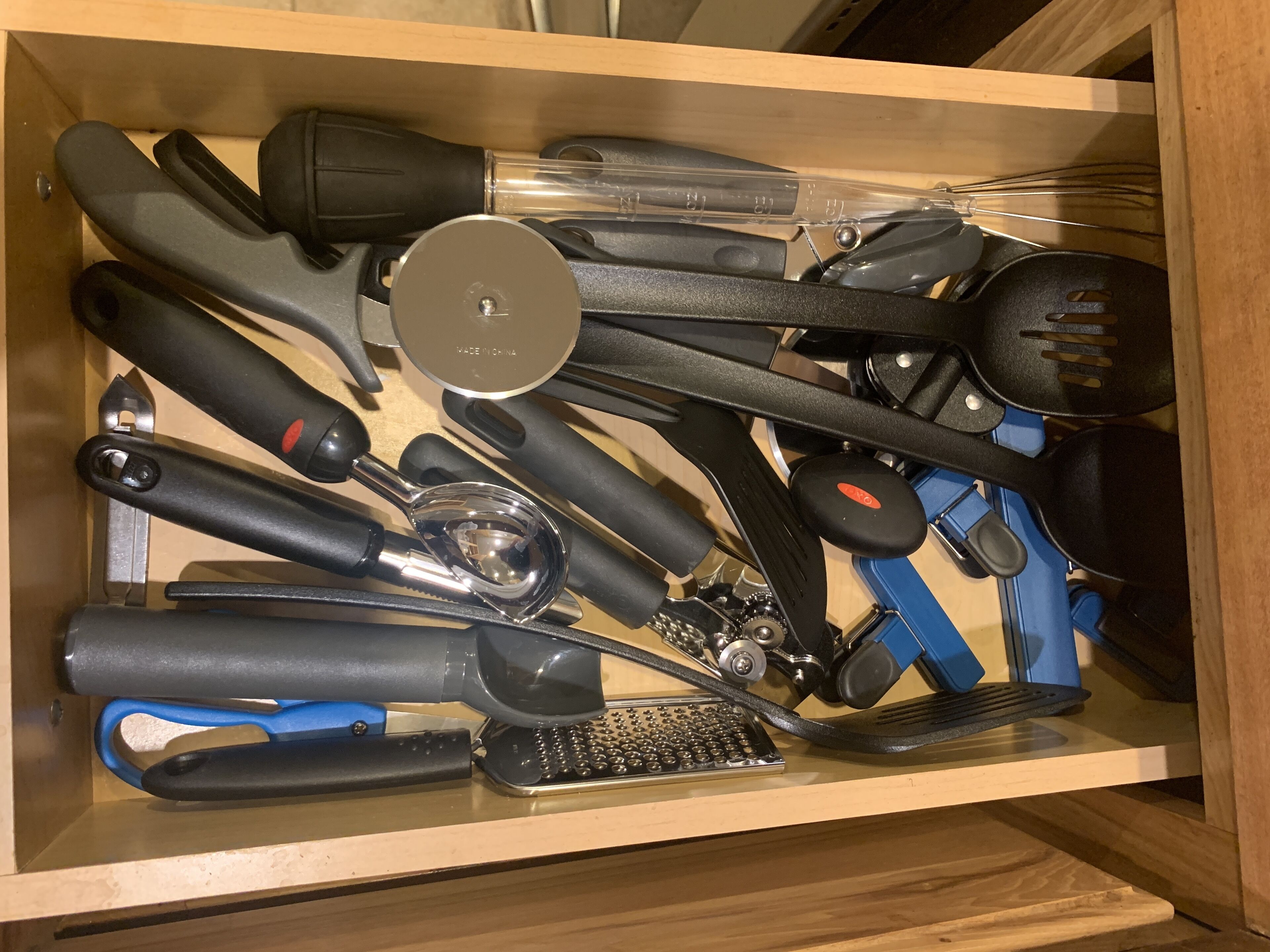 Un tiroir contenant divers ustensiles de cuisine, notamment une râpe, une spatule et une pince.