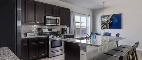 A modern kitchen with dark cabinetry, stainless steel appliances, and a granite countertop island with bar stools.