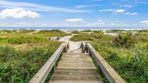 Une promenade en bois qui mène à une plage bordée de dunes, sous un ciel dégagé.