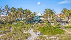 Une propriété située en bord de mer, comprenant une grande maison, des palmiers et une structure dotée d’un toit de chaume.