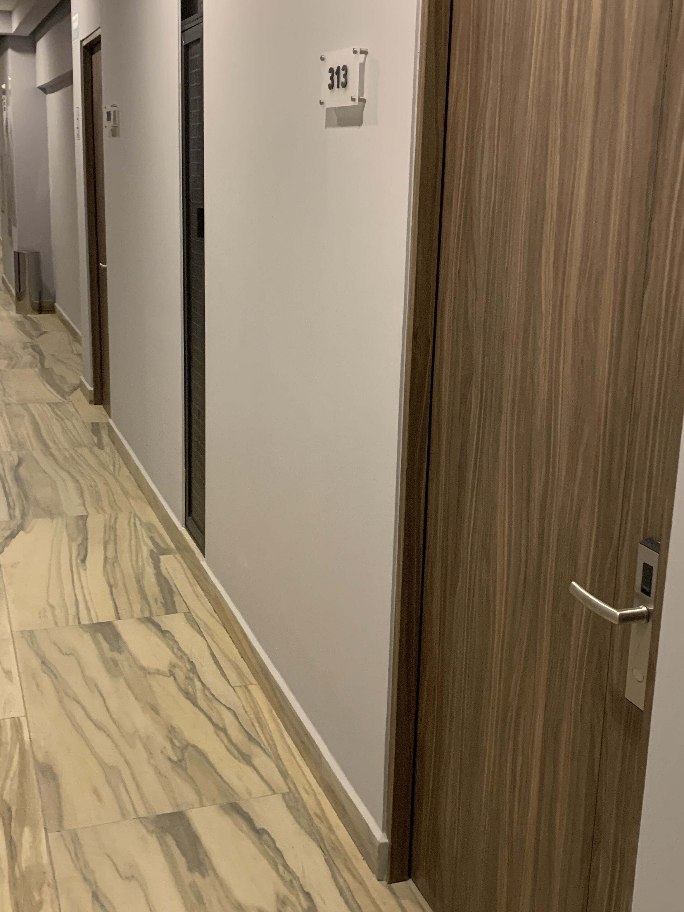 A hallway with a marble floor, a wooden door with a number sign, and a door handle.