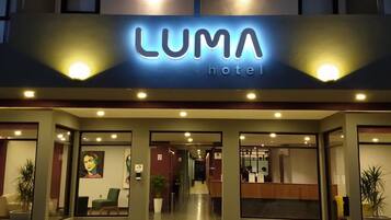 Ein Hotel Eingang mit einem Schild, auf dem 'LUMA hotel' steht, sowie ein Empfangsbereich mit einer Theke und Sitzgelegenheiten.